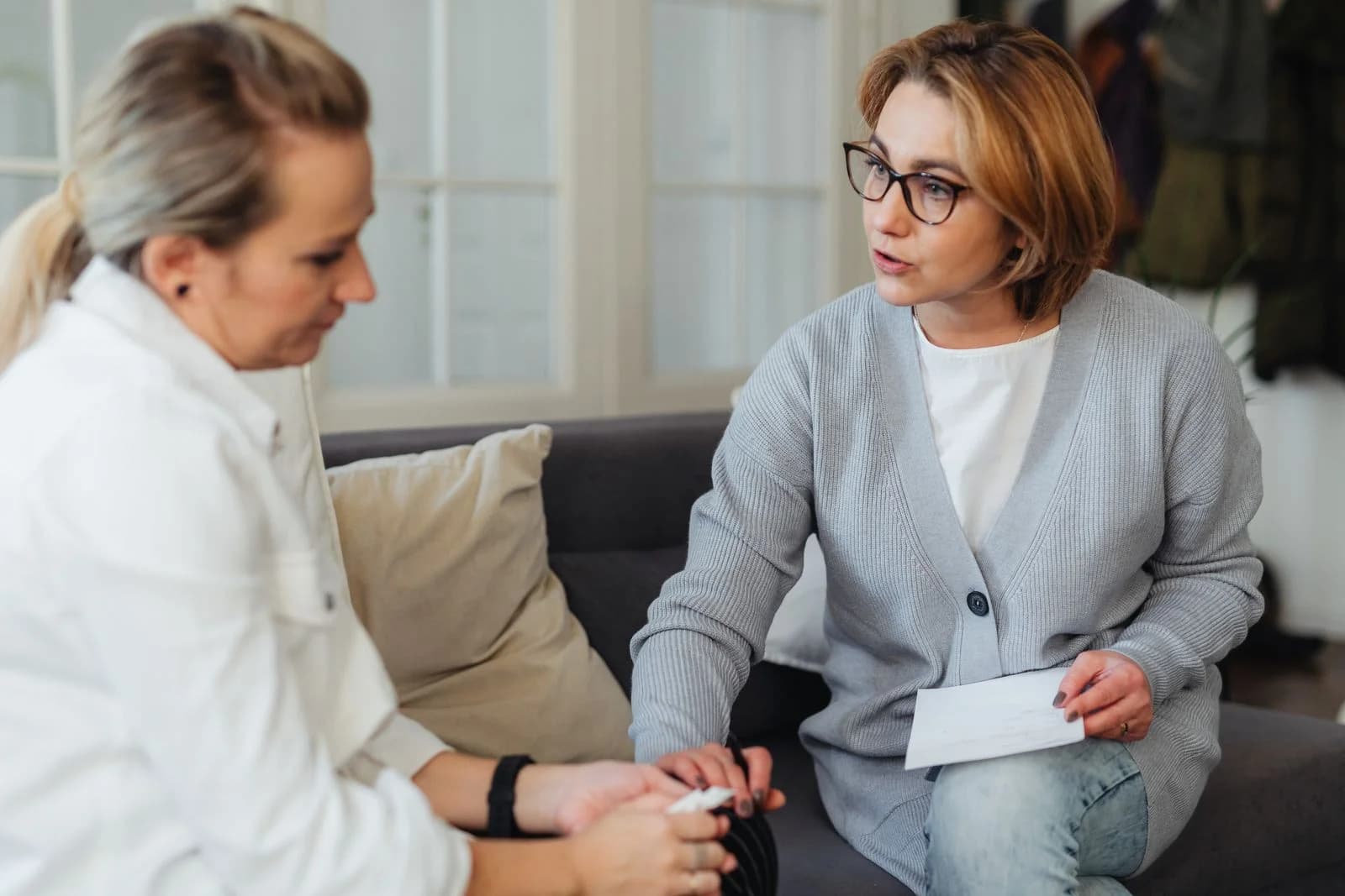 Duas mulheres adultas sentadas dentro de casa tendo uma conversa reflexiva no sofá, ilustrando alternativas não-hormonais à TRH