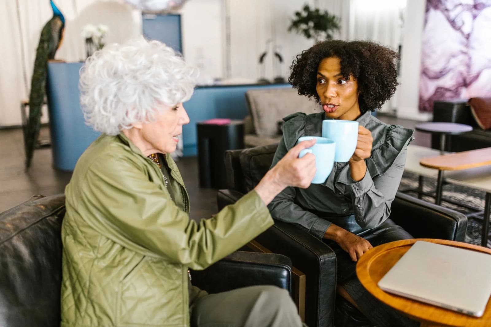 Duas mulheres conversando amigavelmente sobre café em um elegante lounge de escritório, ilustrando amizades intergeracionais
