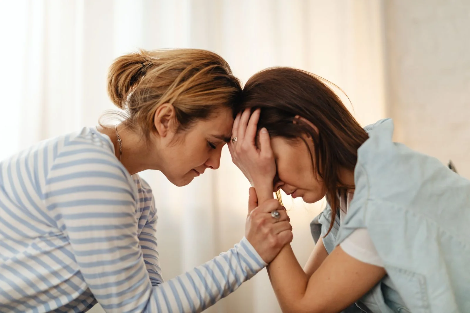 Two women comfort each other in a moment of emotional support indoors, ilustrando como apoiar uma amiga em sofrimento emocional