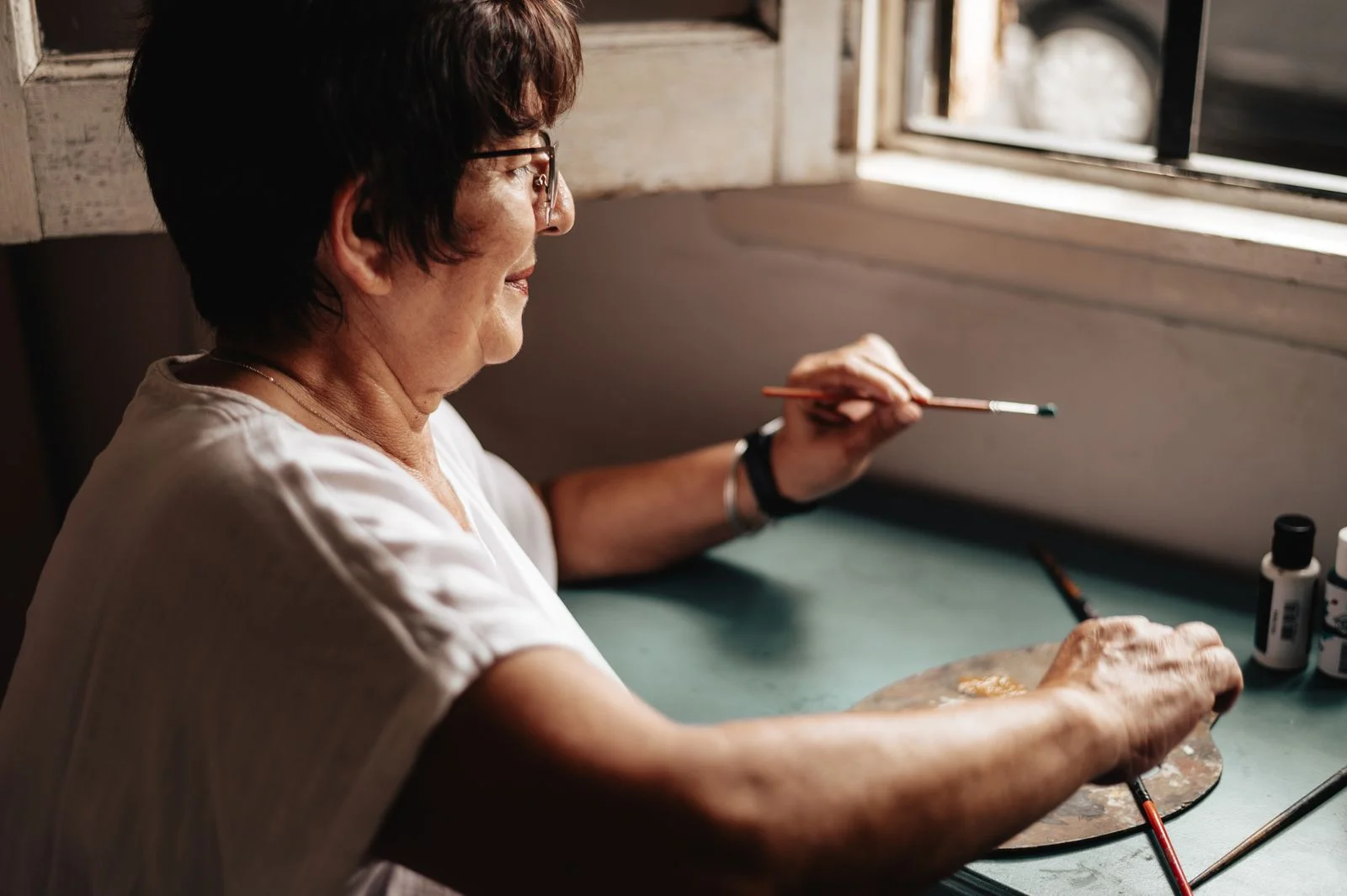 A senior woman enjoys painting near a window, illustrating creativity and leisure, ilustrando aprender algo novo depois dos 40
