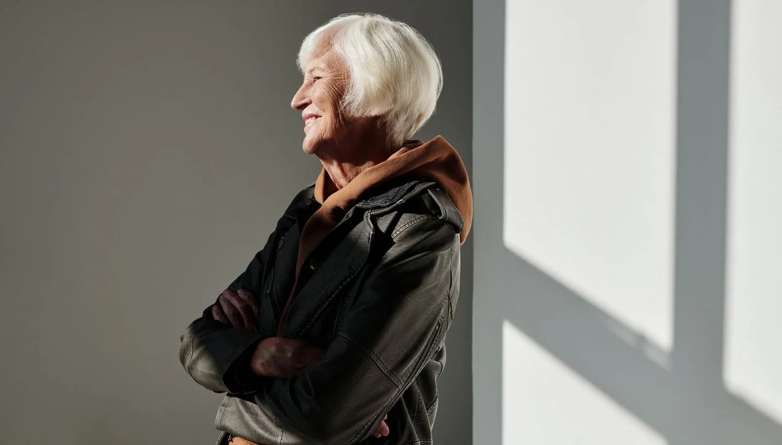 Mulher idosa com jaqueta de couro preta sorrindo confiantemente em ambientes internos, abraçando a moda estilosa, ilustrando a decisão de assumir os cabelos brancos