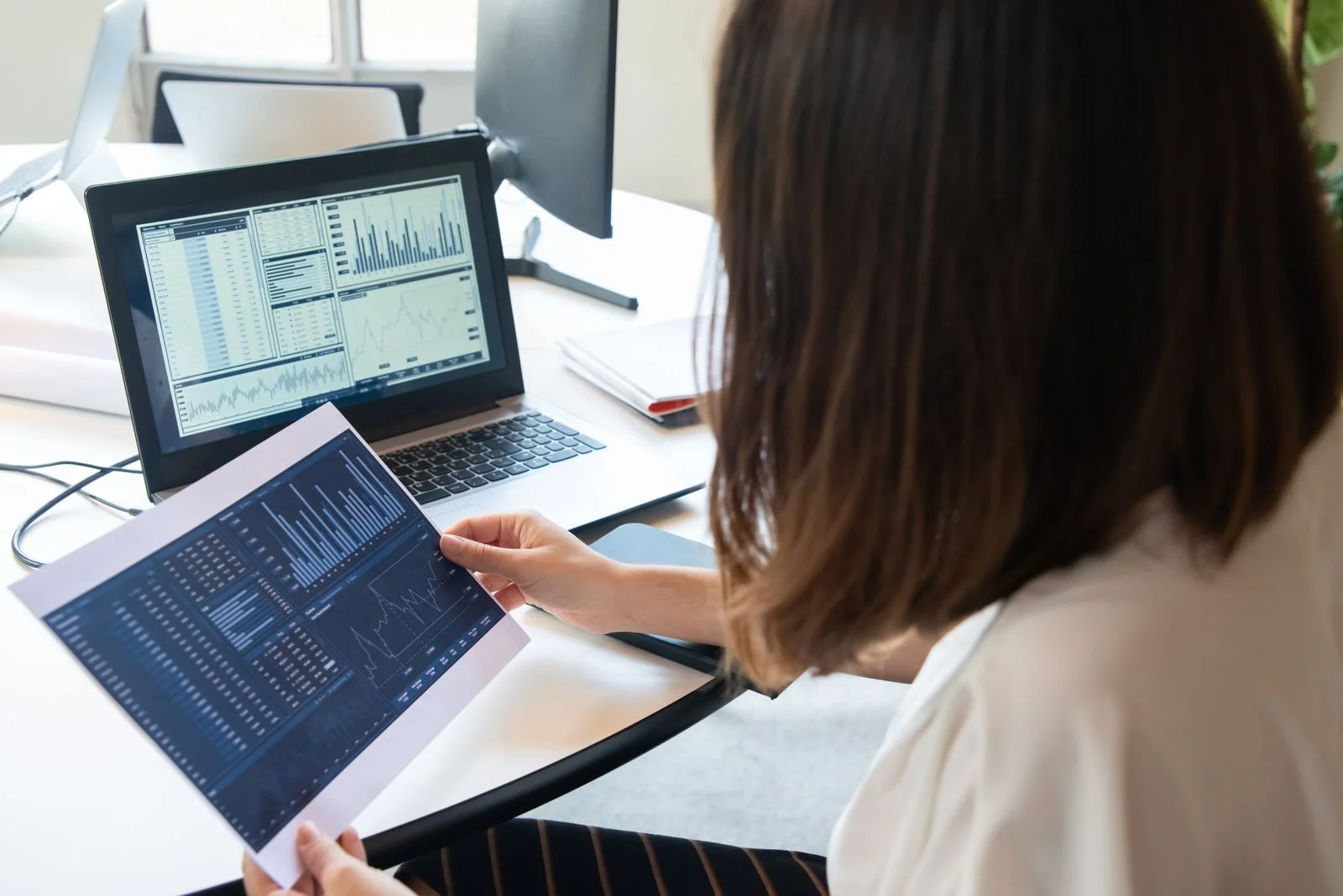 Uma mulher profissional analisa gráficos financeiros em um laptop e em papel para insights de negócios, ilustrando a diferença salarial entre homens e mulheres