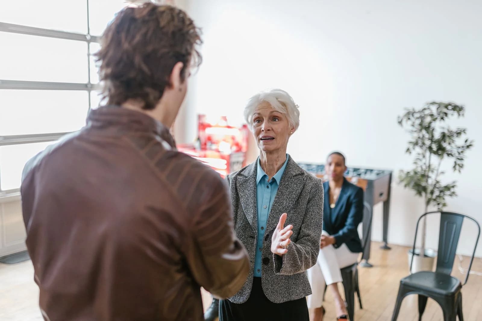 Senior woman engaging in a business discussion indoors with colleagues, ilustrando a dificuldade de aceitar reconhecimento na síndrome da impostora