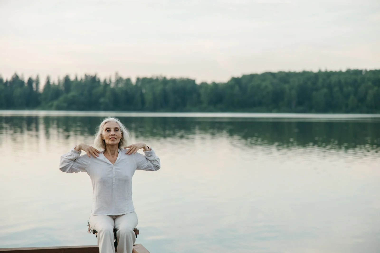 Uma mulher idosa praticando yoga à beira de um lago sereno, promovendo um envelhecimento saudável, ilustrando espiritualidade em momentos de transição