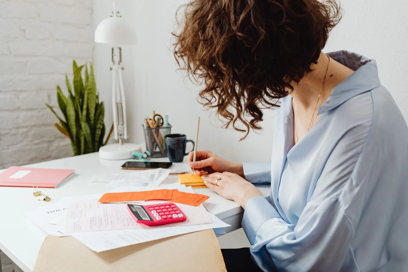 Mulher escrevendo com calculadora na mesa, gerenciando finanças dentro de casa, ilustrando finanças do divórcio depois dos 40