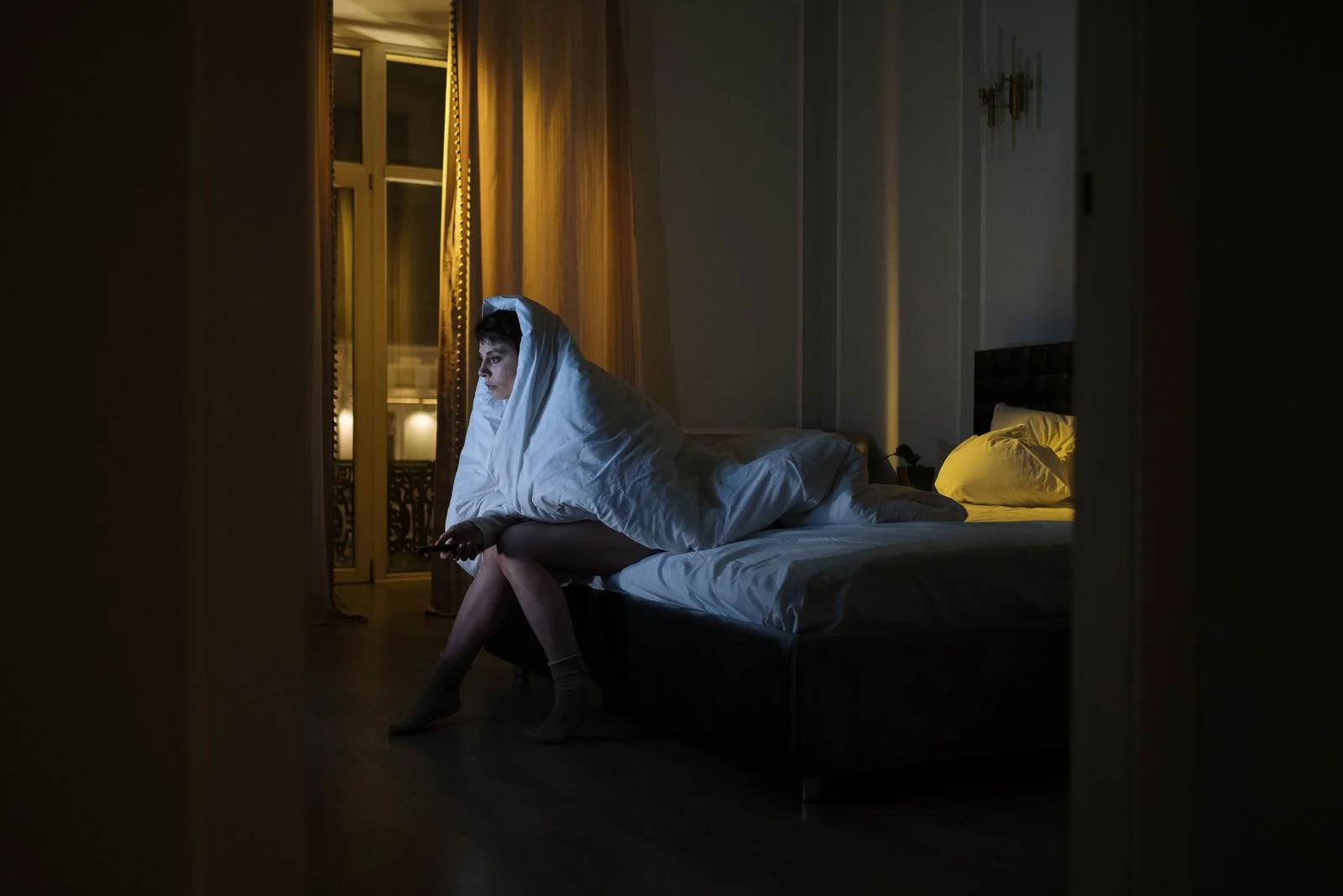Mulher envolta em um cobertor assistindo TV, lutando contra a insônia em um quarto com pouca luz, ilustrando fogachos noturnos na menopausa