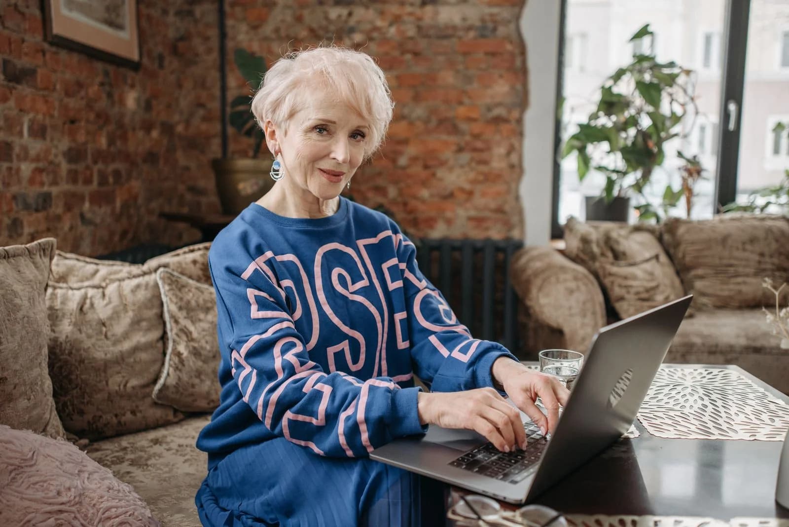 Mulher idosa com cabelo branco usando um laptop em ambiente interno, desfrutando de um espaço de trabalho acolhedor e estiloso, ilustrando síndrome da impostora no recomeço de carreira