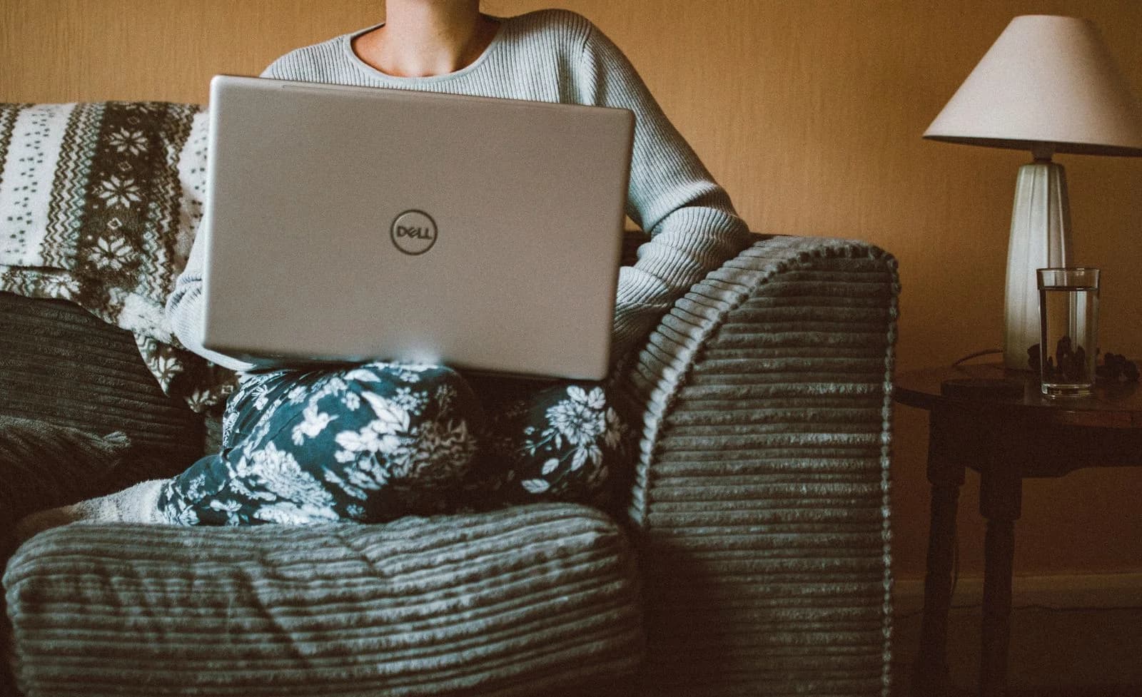Uma mulher vestindo roupas casuais trabalha em um laptop enquanto relaxa em um sofá aconchegante dentro de casa, ilustrando estratégias para lidar com a insônia da menopausa no ambiente profissional