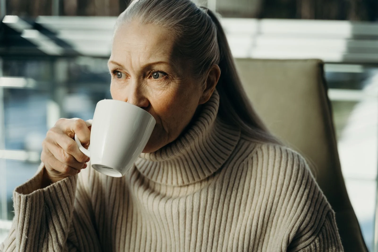 Elderly woman savoring a hot beverage indoors, in cozy attire, ilustrando o que é slow living na prática