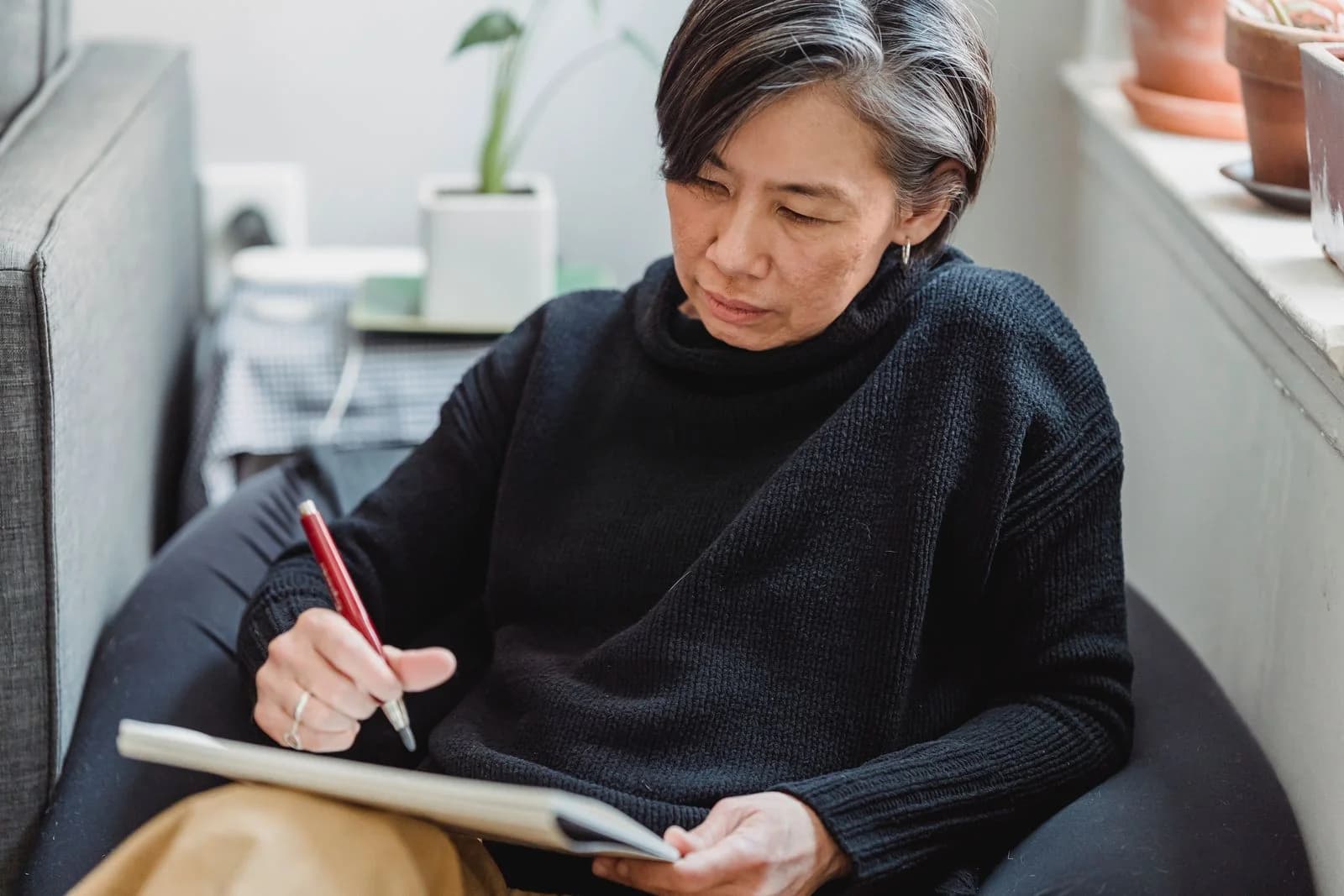 Uma mulher senta-se confortavelmente dentro de casa esboçando em um caderno, abraçando a criatividade, ilustrando perguntas para descobrir o propósito nesta nova fase da vida