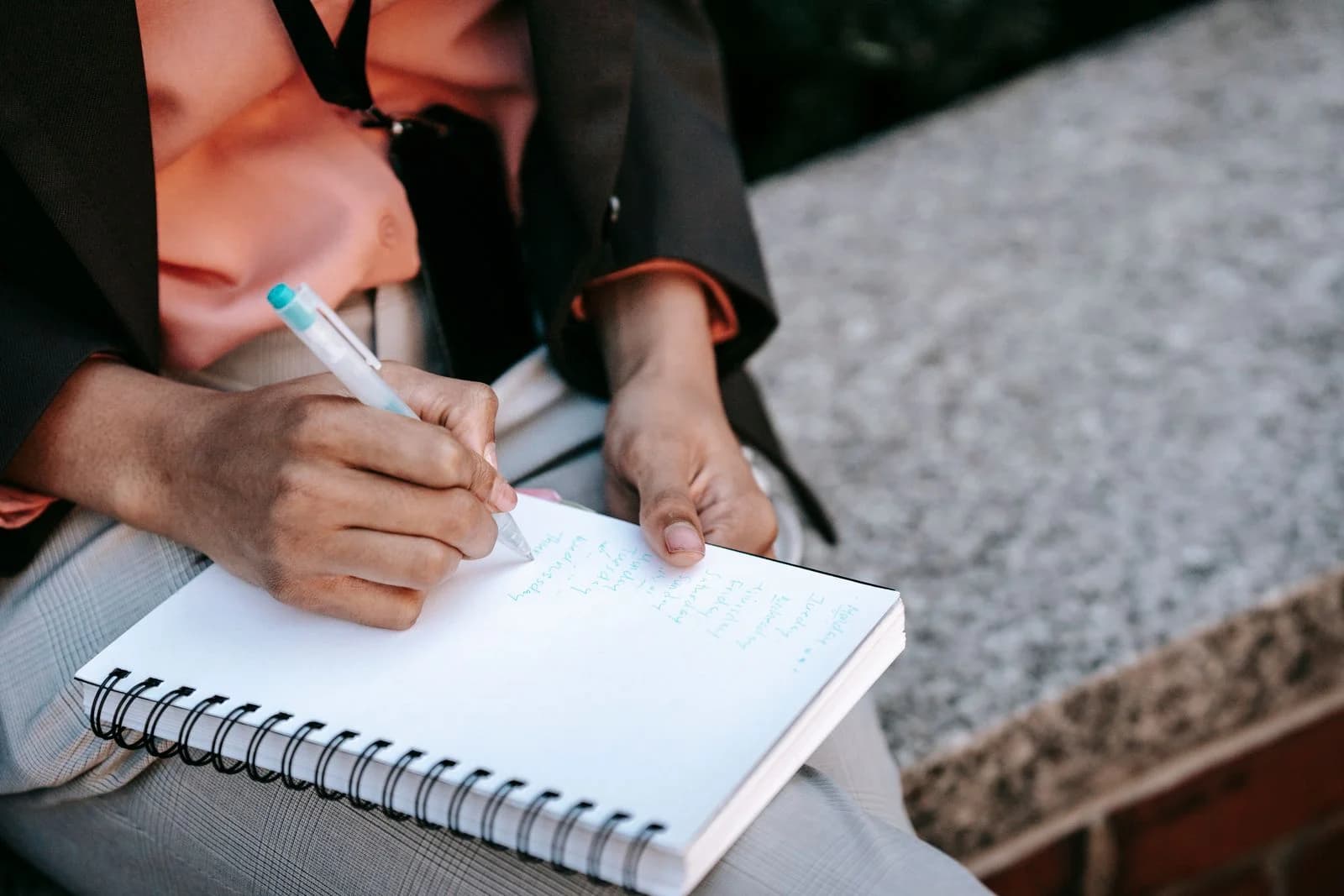 Uma mulher de negócios não reconhecível escreve em um caderno ao ar livre, concentrada no planejamento de seu trabalho, ilustrando o que perguntar quando a insônia da menopausa não melhora