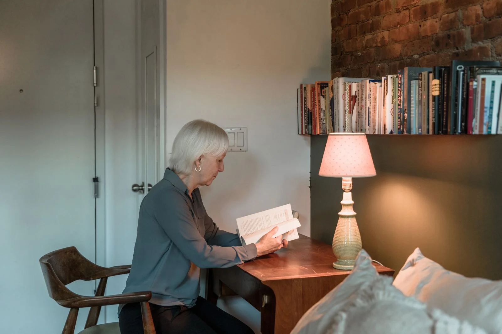 Mulher idosa lendo um livro ao lado de uma lâmpada em um ambiente acolhedor, ilustrando a solidão depois que os filhos saem de casa