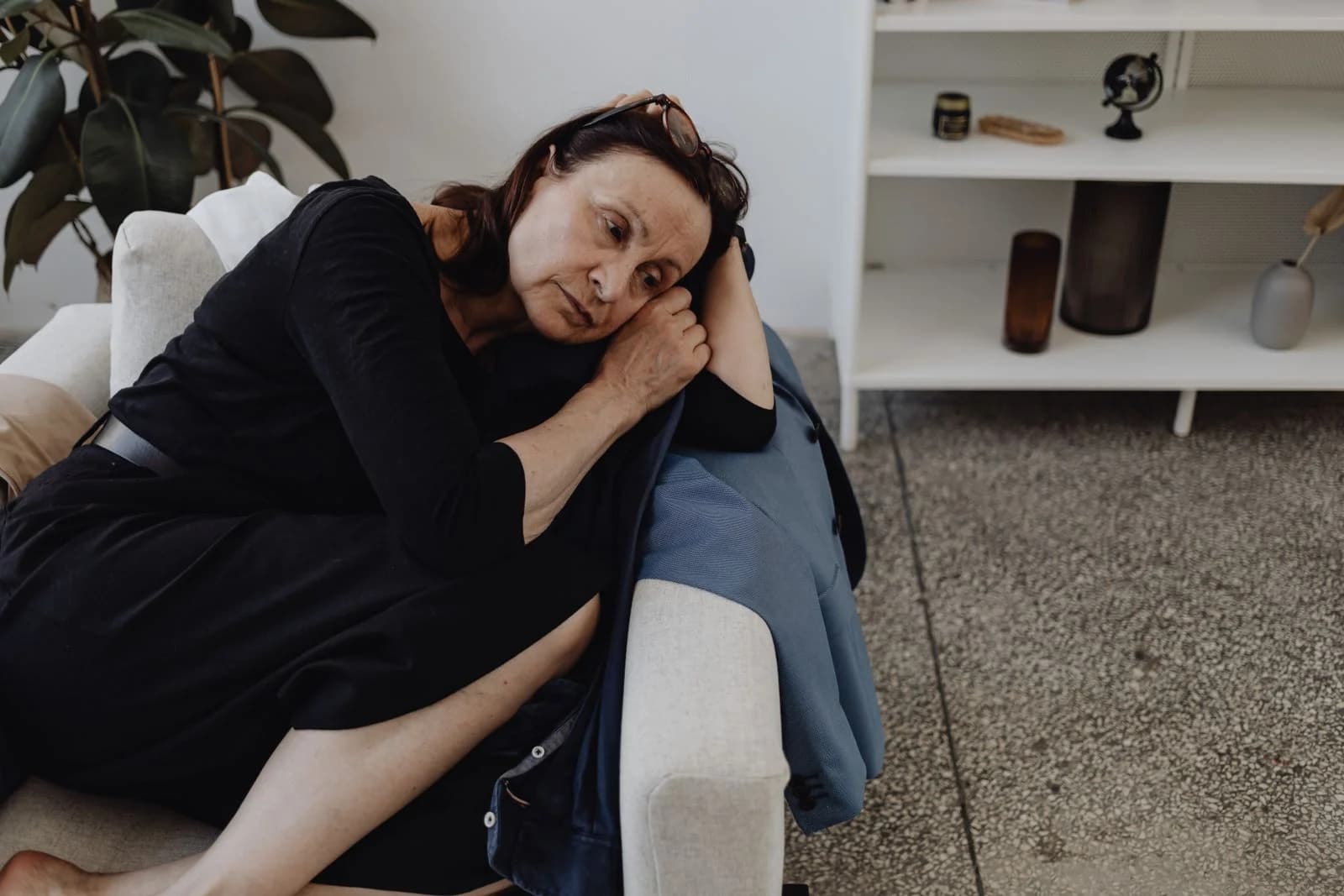 Mulher idosa em profunda reflexão, sentada sozinha em um sofá dentro de casa, ilustrando sinais de que a solidão está afetando a saúde física
