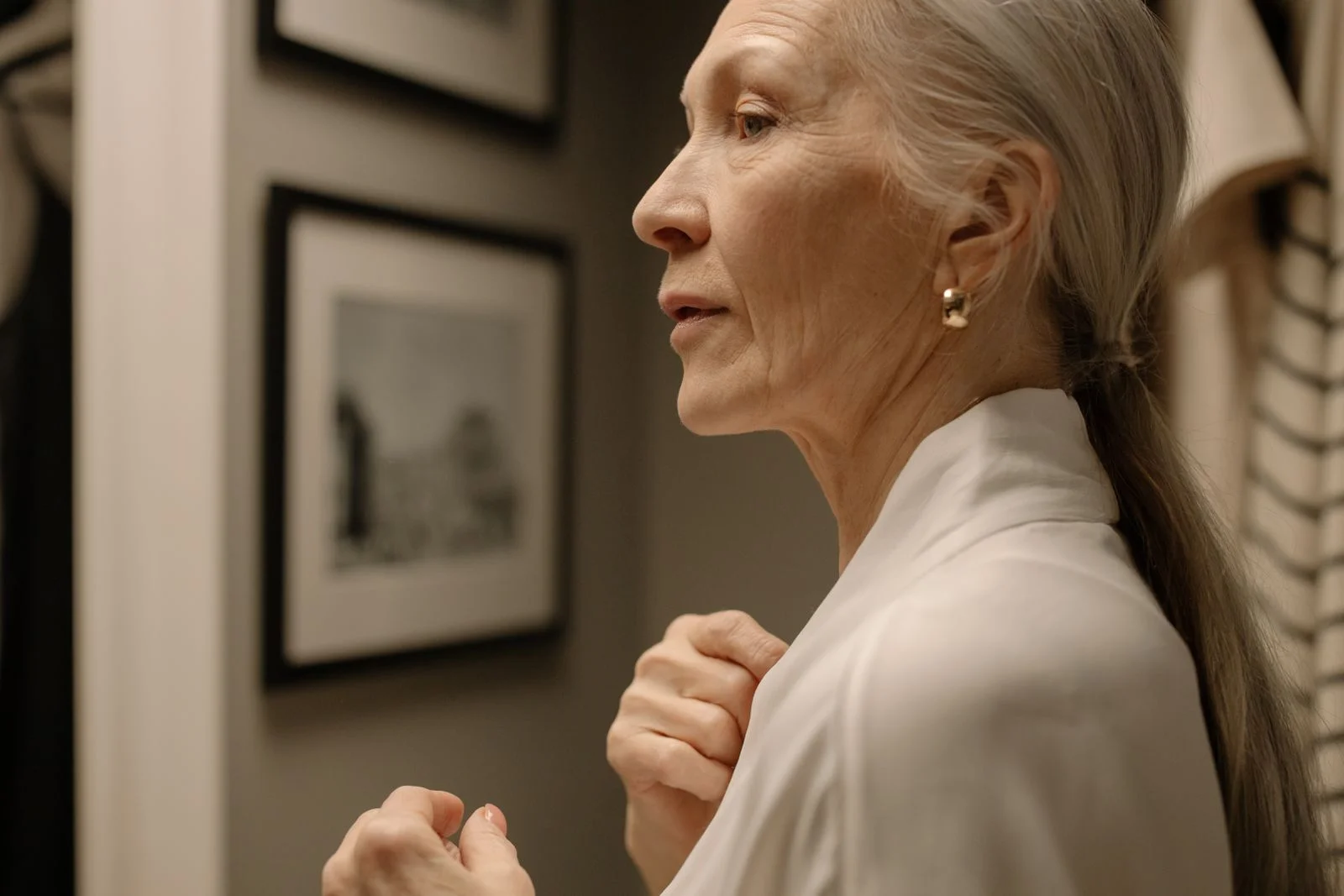 Elegante mulher idosa de perfil usando um robe com joias, em um ambiente interno, ilustrando vestir-se por si mesma