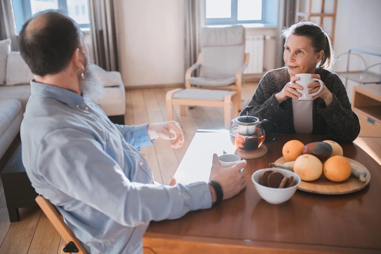 Um casal sênior desfrutando de uma manhã relaxante com chá e frutas em uma sala de estar aconchegante — ajudar financeiramente filhos adultos