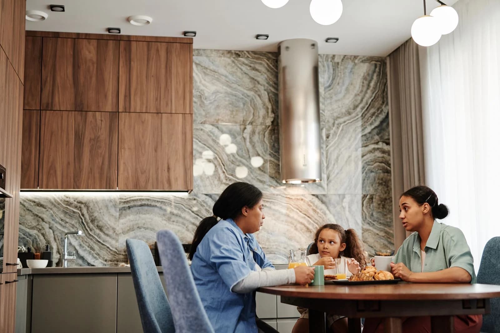 Duas mulheres e uma menina conversam à mesa da cozinha no café da manhã, ilustrando o diálogo em família sobre o humor na perimenopausa