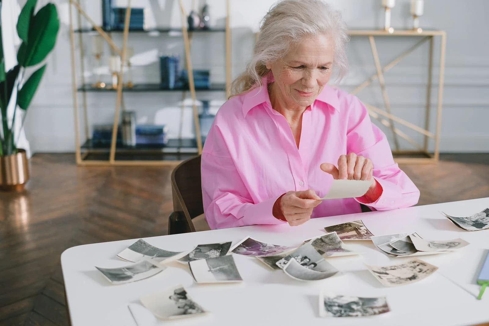 Uma mulher idosa relembrando memórias passadas ao olhar fotografias antigas em uma mesa, ilustrando quando os filhos não correspondem às expectativas