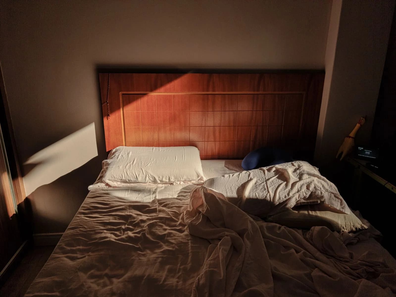 Uma cama desfeita iluminada pelo sol com uma cabeceira de madeira cria uma atmosfera aconchegante e quente, ilustrando higiene do sono adaptada à perimenopausa