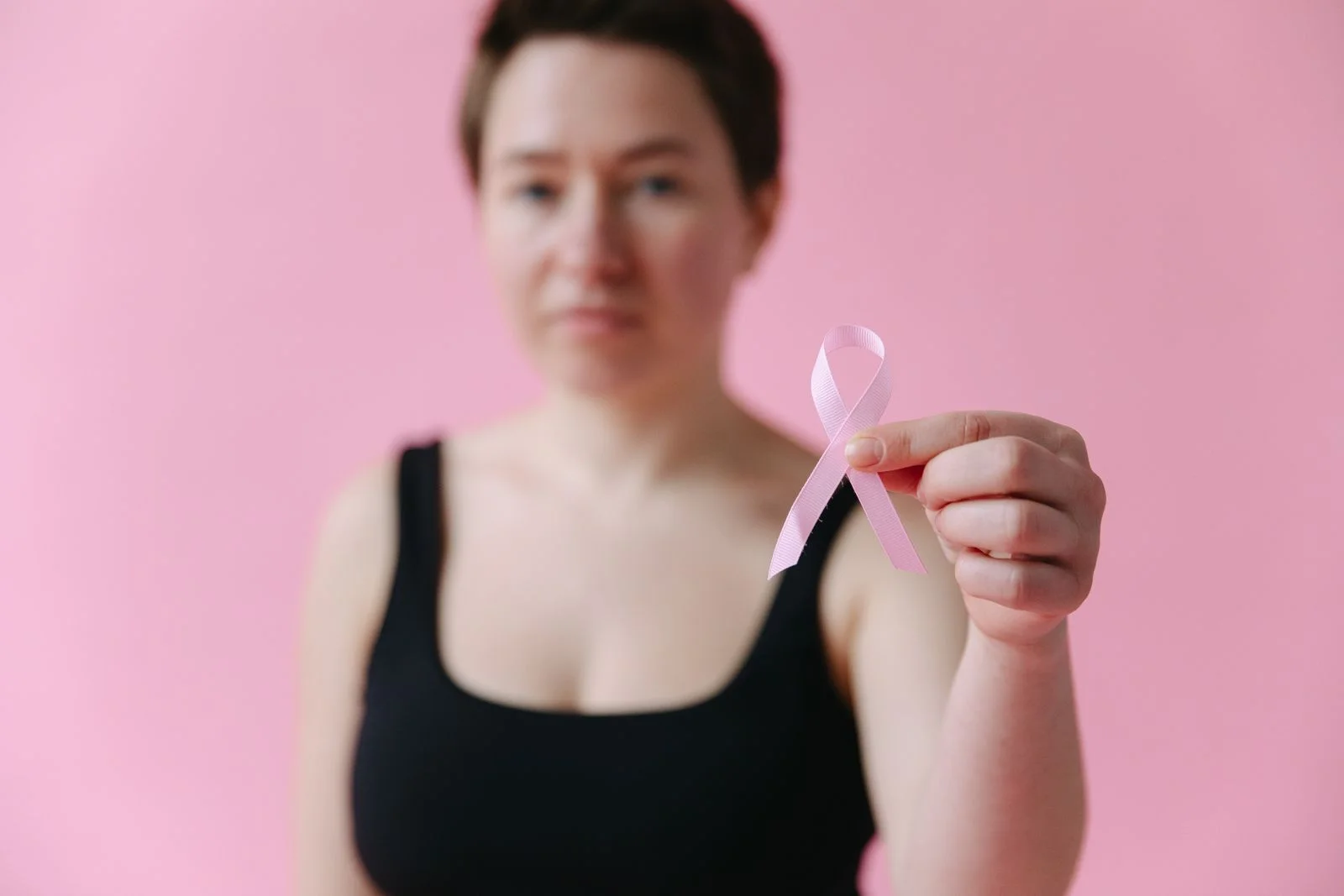 Mulher segura um laço rosa de conscientização sobre o câncer de mama diante de fundo rosa, lembrando a mamografia no Outubro Rosa