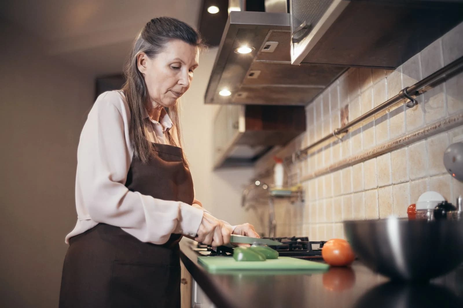Mulher idosa cortando legumes em um ambiente de cozinha quente e aconchegante. Engajada na culinária diária em casa, ilustrando metabolismo na menopausa