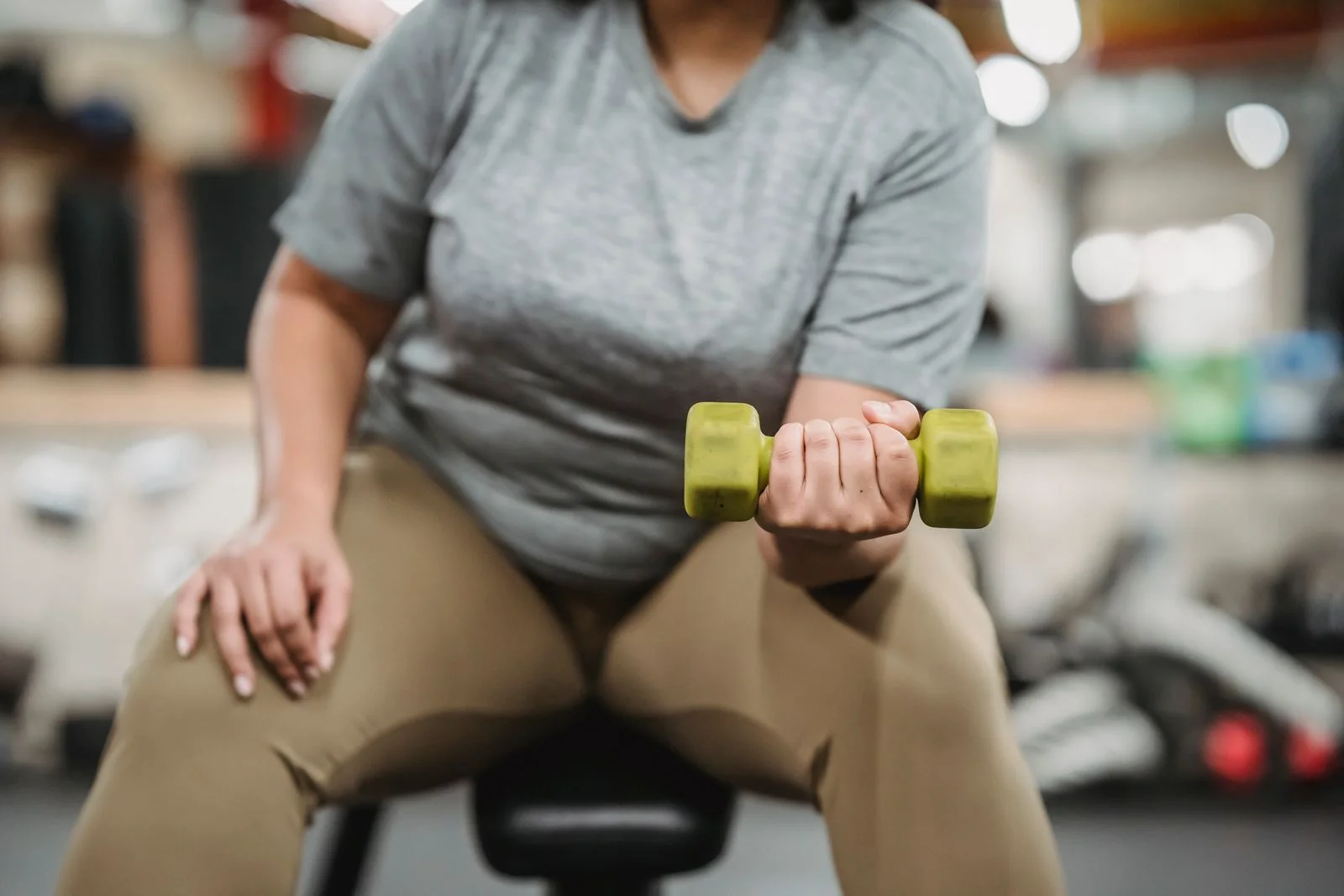 Mulher sentada em banco de academia faz exercício com halter leve, começando a musculação aos 51