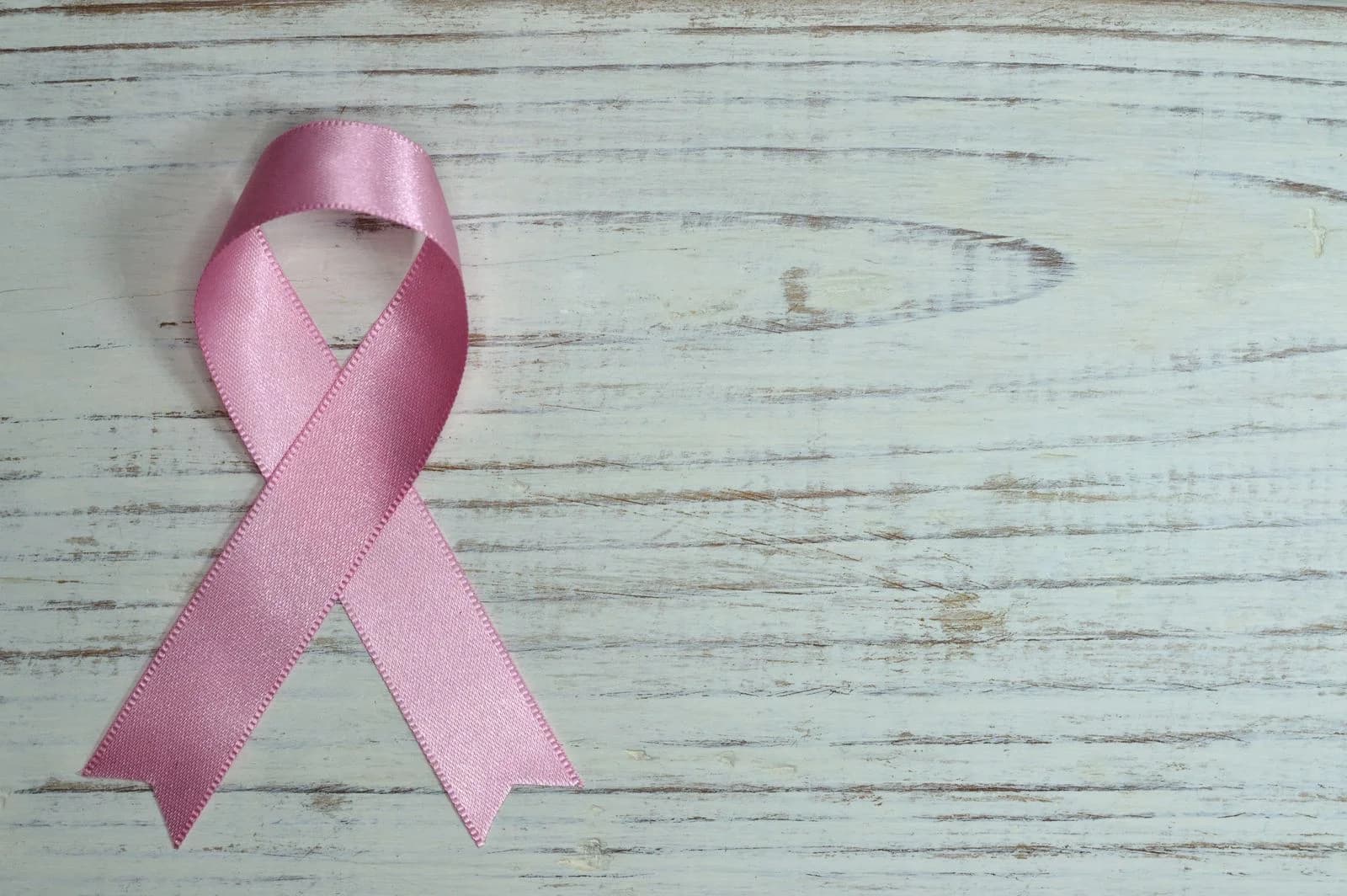 Um laço rosa simbolizando a conscientização sobre o câncer colocado sobre um fundo de madeira clara — incentivar a fazer mamografia