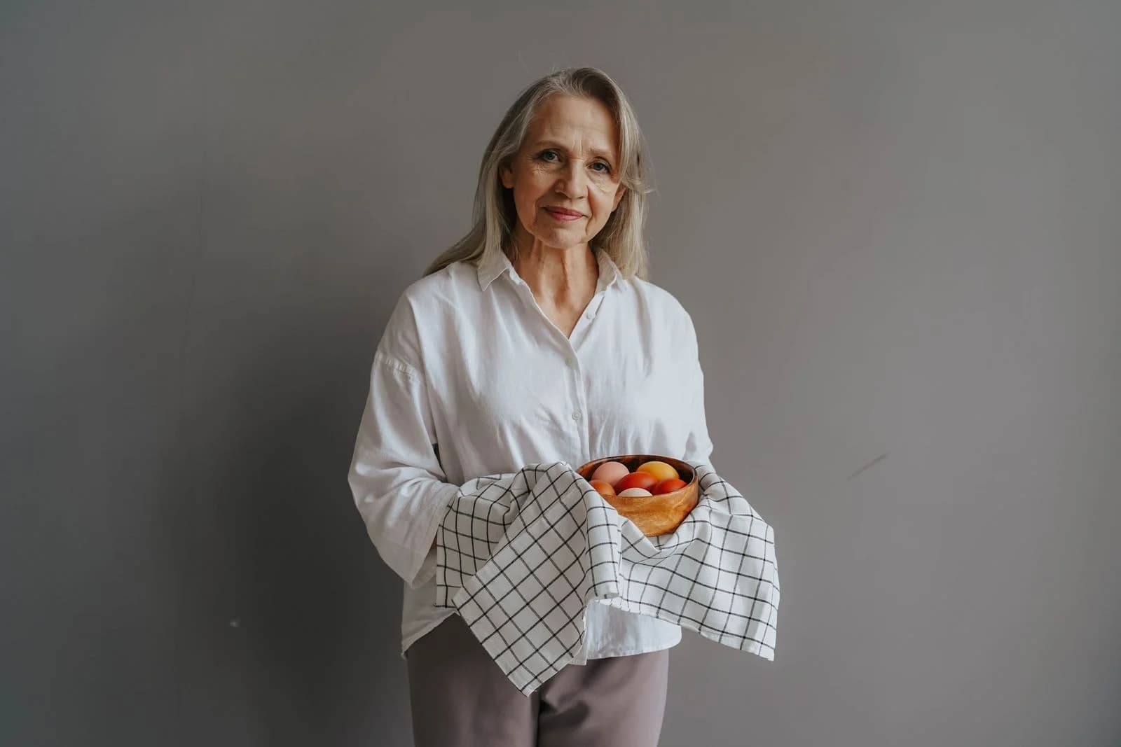 Mulher madura sorri segurando uma tigela de ovos na cozinha, fonte de proteína na menopausa