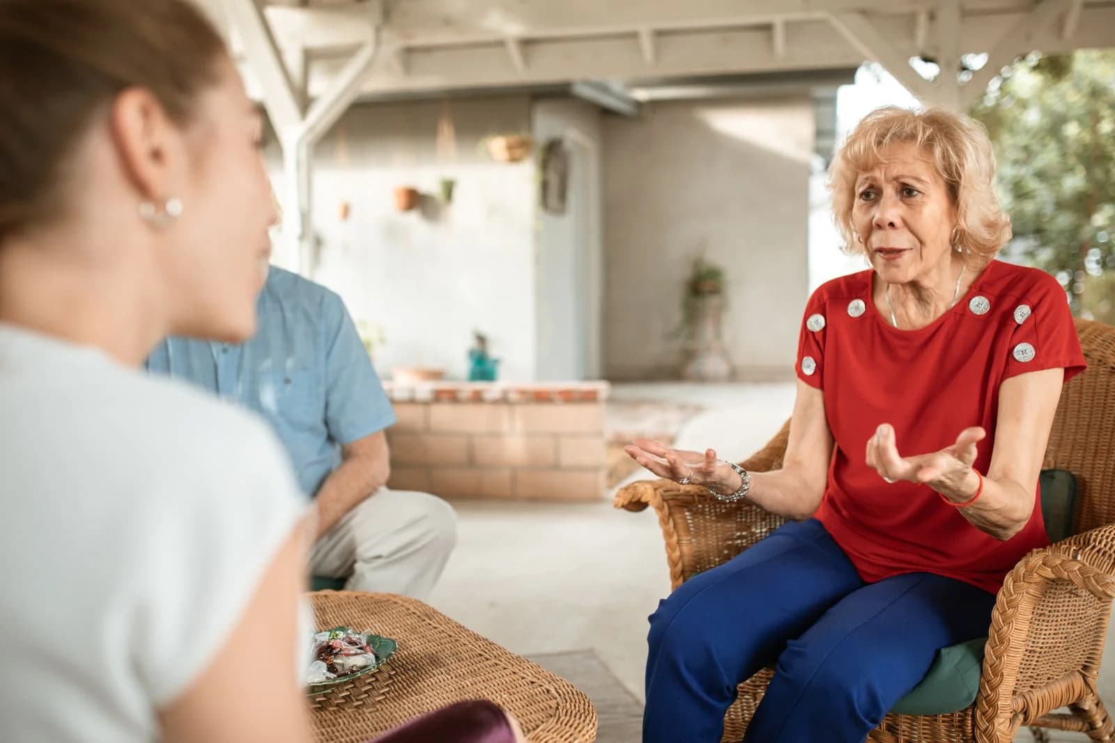 Mulher idosa com camisa vermelha conversando expressivamente com outra mulher em um ambiente aconchegante, ilustrando o relato de reconstruir amizades depois de mudar de cidade
