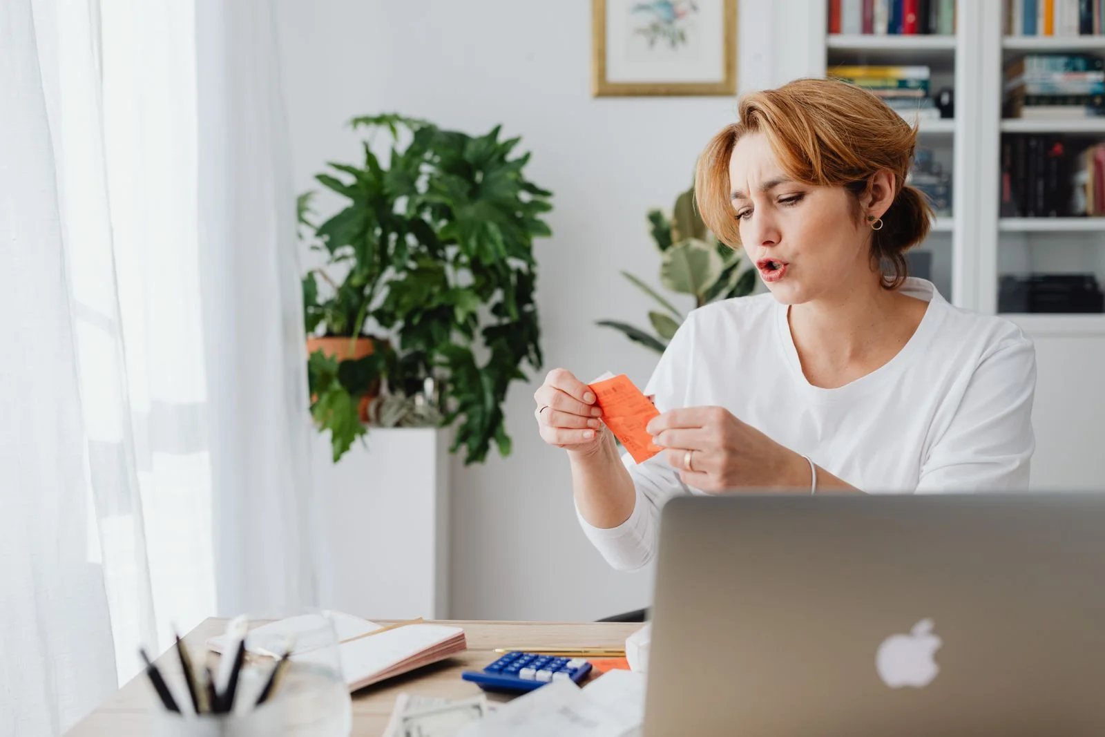 Mulher revisa contas à mesa de casa com notebook e plantas, organizando sua reserva financeira pessoal