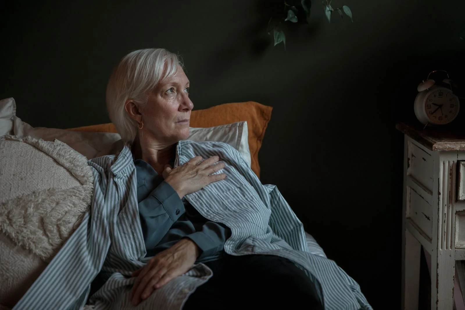 Uma mulher idosa com cabelos brancos parece contemplativa enquanto está reclinada em casa, transmitindo introspecção e calma, ilustrando sinais físicos da oscilação de humor na perimenopausa