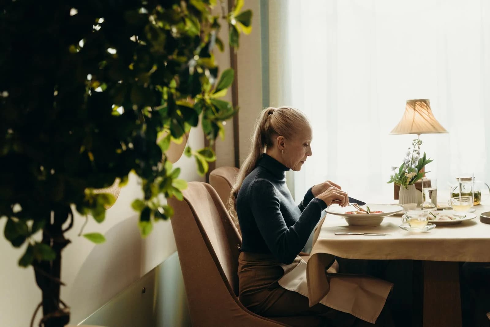 Mulher idosa desfrutando de uma refeição em um ambiente de restaurante interno decorado com bom gosto — slow living nas refeições